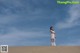 A woman in a white dress standing on top of a sand dune.