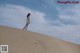 A woman in a white dress standing on top of a sand dune.