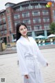 A woman wearing a white bathrobe standing in front of a building.